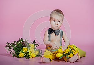 Cute baby boy with spring flowers barefoot in pants in black bow-tie on pink background