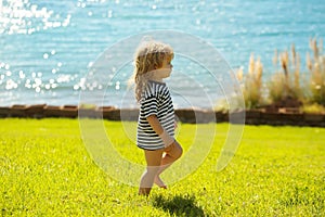 Cute baby boy in striped tshirt walks on green grass