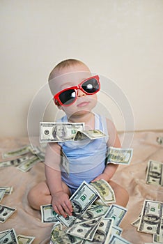 Cute baby boy in sunglasses playing with money, hundreds of dollars