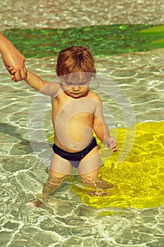 Cute baby boy swims in outdoor pool with mothers help