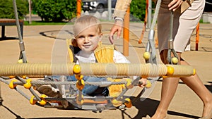 Cute baby boy swinging with mother in spider web swing on playground. Children playing outdoor, kids outside, summer holiday and