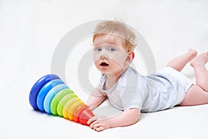 Cute baby boy with toy pyramid on light background
