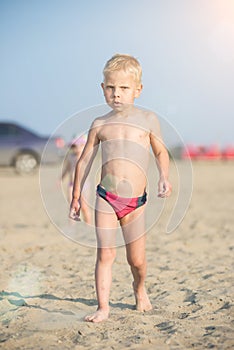 Cute baby boy walking on sandy beach near the sea. Ocean coast.