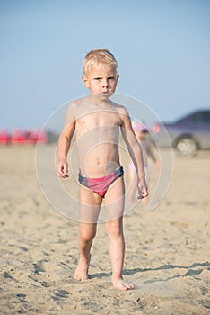 Cute baby boy walking on sandy beach near the sea. Ocean coast.