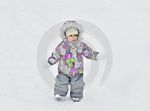 Cute baby boy walking through winter park covered with snow