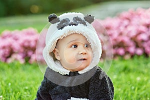 Cute baby boy wearing a Panda bear suit sitting in grass and flowers at park.