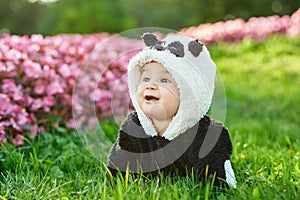 Cute baby boy wearing a Panda bear suit sitting in grass and flowers at park.