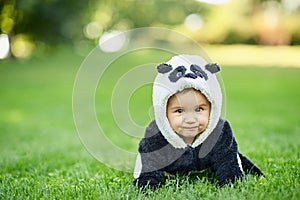 Cute baby boy wearing a Panda bear suit sitting in grass at park.