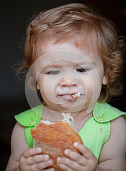 Cute baby with bread in her hands eating. Cute toddler child eating sandwich, self feeding concept. Funny child face.