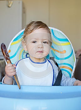 Cute baby child getting messy eating cereals or porridge by itself, with a wooden spoon
