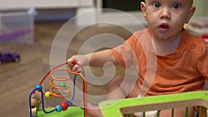 cute baby child in orange shirt playing wooden circle bead maze educational toy