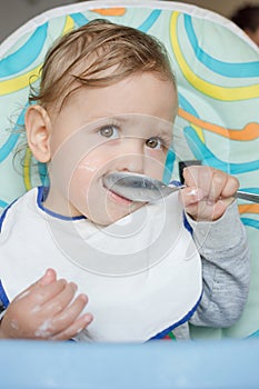 Cute baby child portrait getting messy eating cereals or porridge by itself