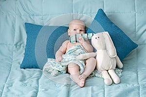 Cute baby closed mouth with hare toy ear on bed. Portrait of a child with emotions