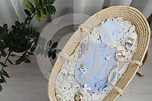 Cute clothes and accessories in basket bassinet at home, top view