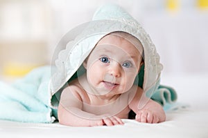 Cute baby covered with a bath towel lying on tummy in the bathroom