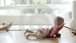 Cute baby crawling on floor from mom to dad and grasping phone