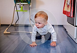 Cute baby crawling on the wood floor in the kitchen at home