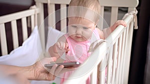 Cute baby in crib touch smartphone. Baby technology concept