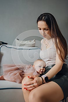 Cute baby daughter in an elegant dress lies on her mother& x27;s knees