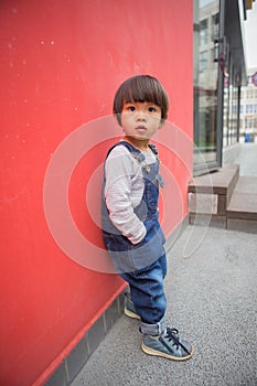 Cute baby in denim overalls posing in front of red wall