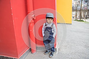 Cute baby in denim overalls posing in front of red wall