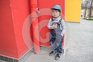 Cute baby in denim overalls posing in front of red wall