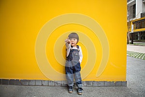 Cute baby in denim overalls posing in front of yellow wall