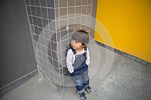 Cute baby in denim overalls posing in front of yellow wall