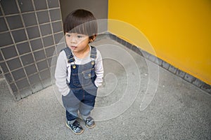 Cute baby in denim overalls posing in front of yellow wall