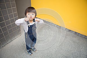 Cute baby in denim overalls posing in front of yellow wall
