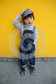 Cute baby in denim overalls posing in front of yellow wall
