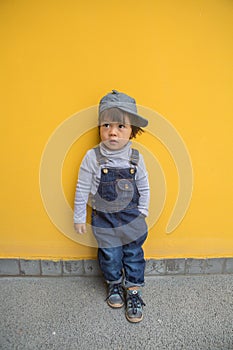 Cute baby in denim overalls posing in front of yellow wall