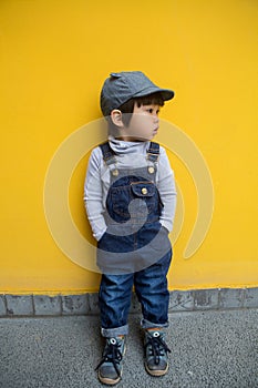 Cute baby in denim overalls posing in front of yellow wall