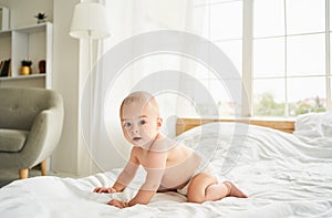 Cute baby in a diaper on the bed in the bedroom