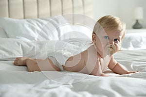 Cute baby in diaper with pacifier lying on bed at home