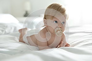 Cute baby in diaper with pacifier lying on bed at home