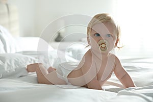 Cute baby in diaper with pacifier lying on bed at home