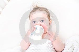 Cute baby drinking milk from a bottle in a white crib