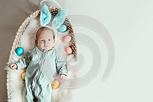 Cute baby Easter bunny. Little baby boy with bunny ears and Easter eggs in wicker basket in white fur. Symbol of Easter holiday,