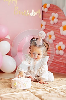 Cute baby eating cake for first birthday. Baby girl in dress. Festive decor in pink colors