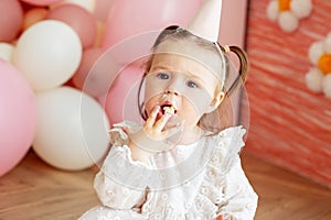 Cute baby eating cake for first birthday. Baby girl in dress. Festive decor in pink colors