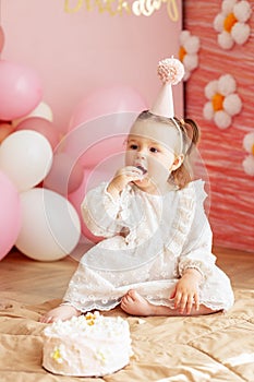 Cute baby eating cake for first birthday. Baby girl in dress. Festive decor in pink colors