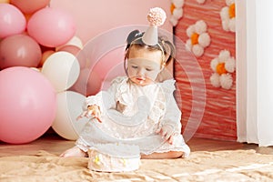 Cute baby eating cake for first birthday. Baby girl in dress. Festive decor in pink colors