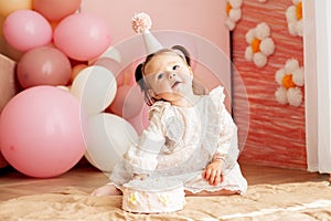 Cute baby eating cake for first birthday. Baby girl in dress. Festive decor in pink colors