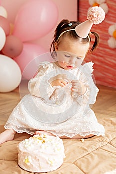 Cute baby eating cake for first birthday. Baby girl in dress. Festive decor in pink colors