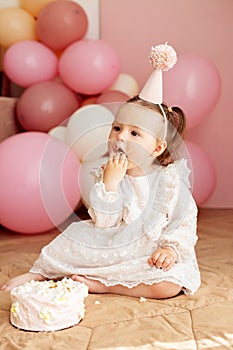 Cute baby eating cake for first birthday. Baby girl in dress. Festive decor in pink colors