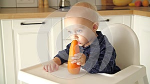 Cute baby eating carrot in a white kitchen. Healthy nutrition for kids. Bio carrot as first solid food for infant