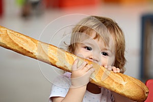 Cute baby eating French baguette white bread. Funny toddler child eating sandwich, self feeding concept.