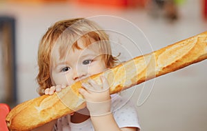 Cute baby eating French baguette white bread. Funny toddler child eating sandwich, self feeding concept.