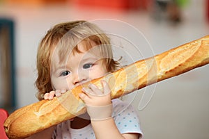 Cute baby eating French baguette white bread. Funny toddler child eating sandwich, self feeding concept.